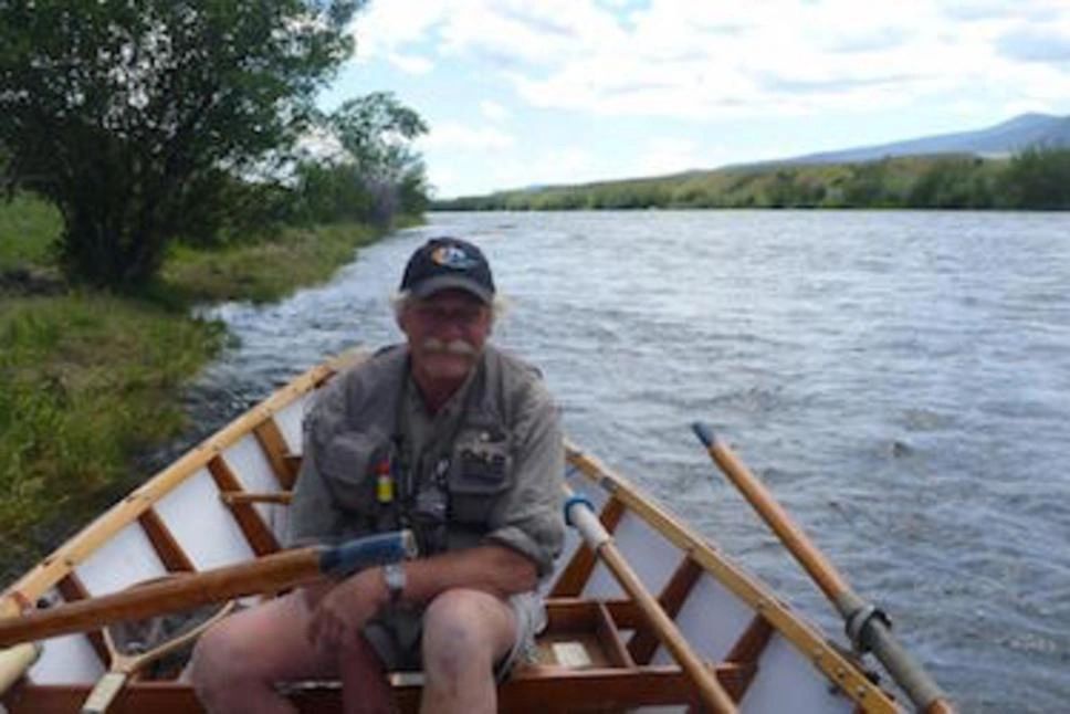 Man fishing from a wooden canoe on a calm river